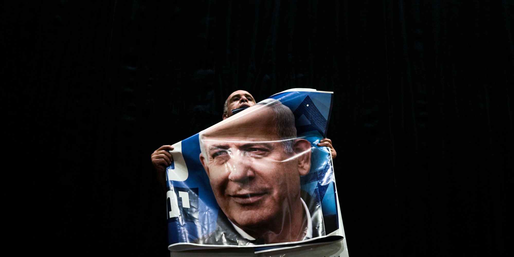 A Likud party supporter holds a poster of the party's head and former Israeli Prime Minister Benjamin Netanyahu as he delivers an election campaign in Migdal Haemek, northern Israel, Sunday, Oct. 23, 2022. Israel is heading into its fifth election in under four years on Nov. 1. (AP Photo/Ariel Schalit)